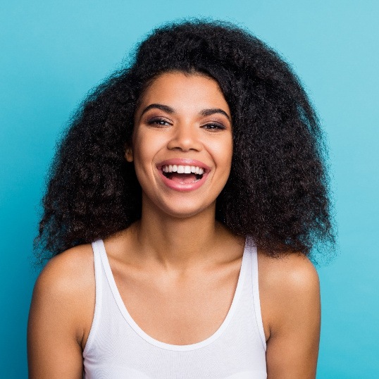 Woman in white tank top smiling in front of light blue background