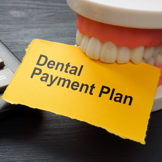 Model teeth holding a yellow paper that says “Dental Payment Plan”