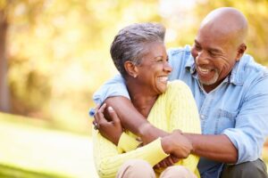 Man in blue shirt hugging woman in yellow sweater from behind outside in the sun